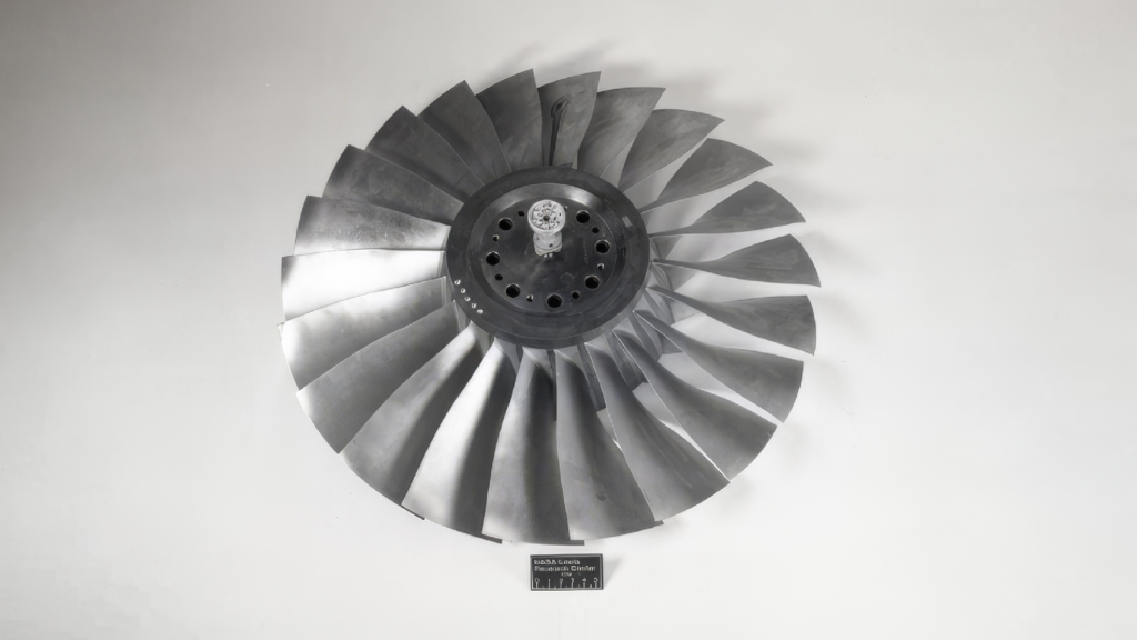 Front view of the NASA Rotor 67 axial compressor rotor geometry, featuring metallic rotor blades arranged around a central hub, used as a benchmark in turbomachinery and CFD research.